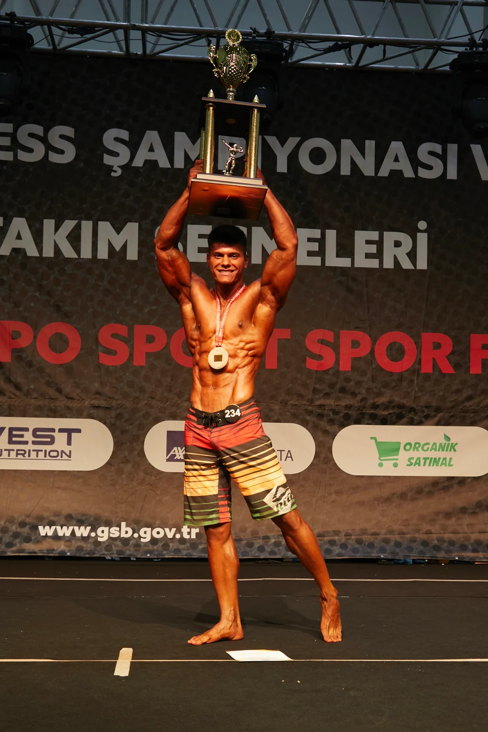 Yarışma sahnesinde kupasını başının üzerinde tutan sporcu.
